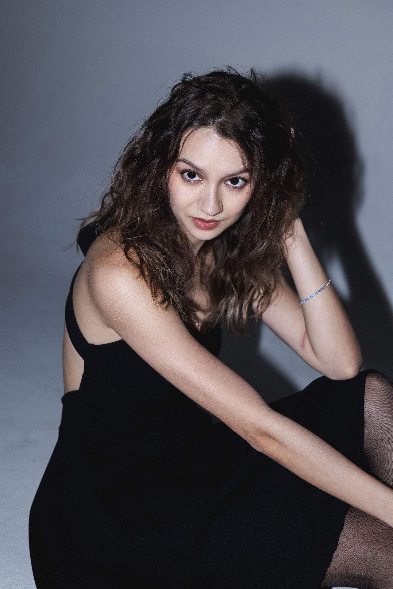 Seated in a black dress and sheer tights