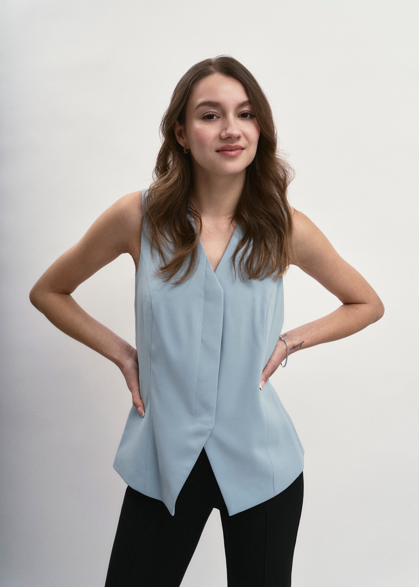 Hands on hips in a pale blue vest
